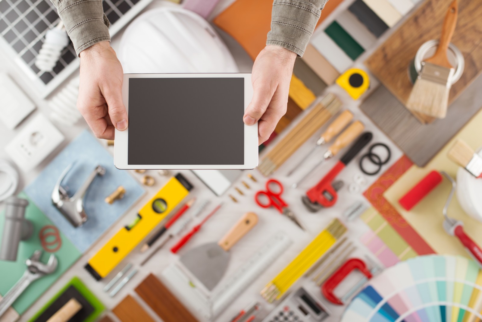 Male hands using a digital tablet, construction and home decoration tools on background, top view, DIY and home improvement mobile app concept